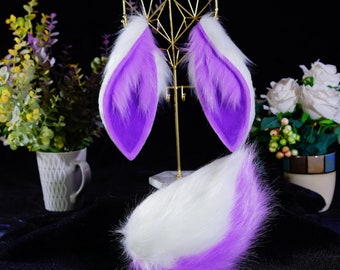 May include: A set of purple and white faux fur cat ears and tail. The ears are attached to a gold metal stand. The tail is lying on a black surface.