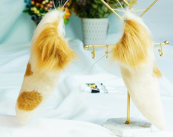 May include: Two fluffy, white and brown faux fur tails with gold tips are displayed on a gold metal stand. The tails are attached to a gold wire headband.