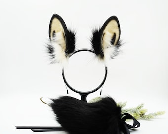 以下が含まれることがあります： 黒と白のフェイクファーの猫耳ヘッドバンドと、黒いフェイクファーの尻尾。ヘッドバンドは黒いスタンドの上に置かれています。