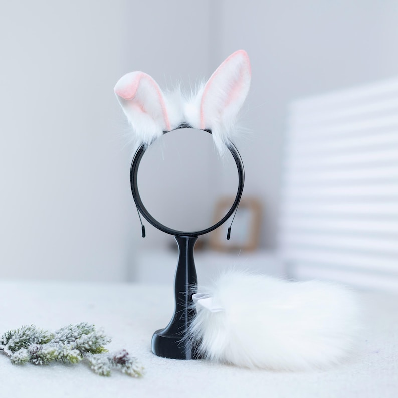 May include: White fluffy bunny ears headband with pink tips, a white fluffy tail, and a black round mirror on a stand.