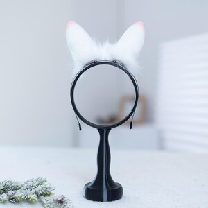 May include: A black tabletop vanity mirror with a white fluffy bunny ear headband on top.