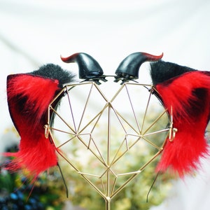 May include: A pair of black and red faux fur devil horns with a gold metal heart-shaped stand.