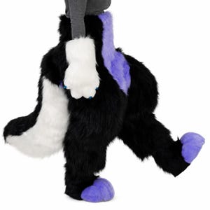 May include: A full-body faux fur costume featuring black, white, and purple sections. The suit includes a large white tail, white paw-style hand coverings with blue claws, and purple paw-style foot coverings. The fur is long and textured throughout.