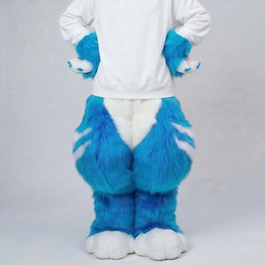 May include: A furry costume with blue and white faux fur. The costume includes blue furry trousers, matching blue furry arm covers, and white paw-like feet. The person is wearing a white sweatshirt.