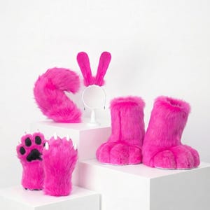 May include: A set of bright pink faux fur costume accessories including a pair of paw-shaped gloves with black pads and white claws, a pair of furry boot covers, a plush tail, and a headband featuring two long, upright rabbit-style ears.