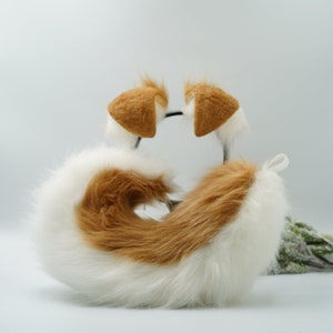 Può includere: Una coda di pelliccia sintetica bianca e marrone soffice con orecchie abbinate in pelliccia sintetica marrone. La coda è arrotolata e le orecchie sono attaccate a una fascia per capelli.