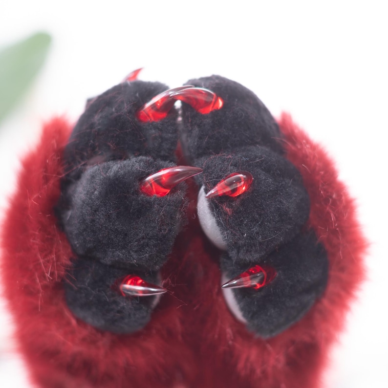 May include: Close-up of a pair of plush black paws with red claws. The paws are surrounded by red fur. The claws are translucent and pointed, giving a fierce appearance.