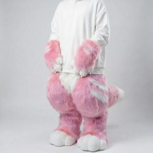 May include: A pink and white furry costume set, including large paw-like gloves and foot covers. The costume has a white and pink color scheme, with a tail visible at the back. The outfit is designed to resemble an animal.