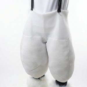 May include: White costume pants with padded legs and black suspenders. The pants have a textured fabric and are worn with white furry boot covers. The costume is likely for a mascot or character.