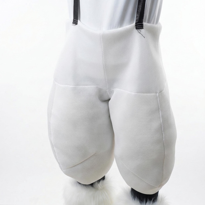 May include: White costume pants with padded legs and black suspenders. The pants have a textured fabric and are worn with white furry boot covers. The costume is likely for a mascot or character.