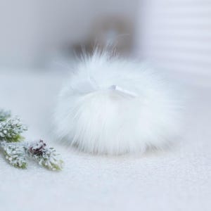 May include: A white fluffy pom pom with a white satin ribbon tied around it.