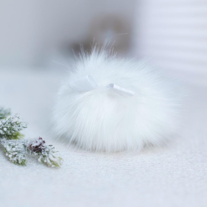 May include: A white fluffy pom pom with a white satin ribbon tied around it.