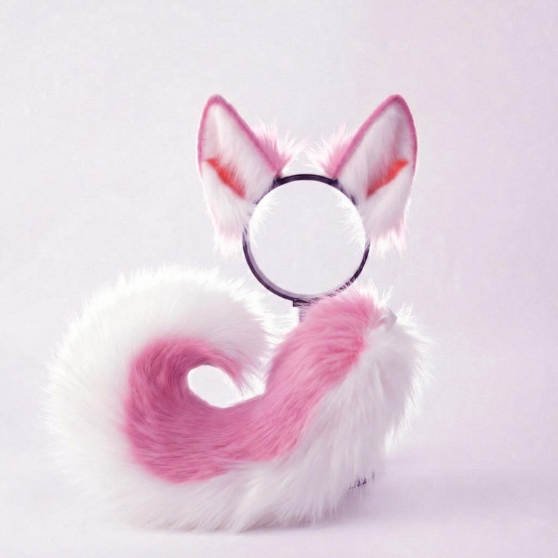 Op de afbeelding: Een cosplay-set met witte en roze vossenoren op een zwarte hoofdband en een bijpassende staart. De oren hebben roze en rode details. De staart is wit met een roze middengedeelte, ontworpen voor kostuumgebruik.