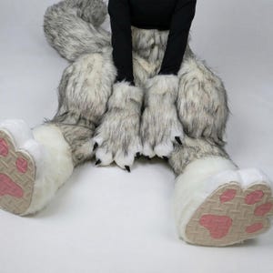 May include: A furry costume featuring large, plush wolf paws with pink paw pads and black claws. The costume includes matching leg coverings in shades of gray and white, with a long, fluffy tail.