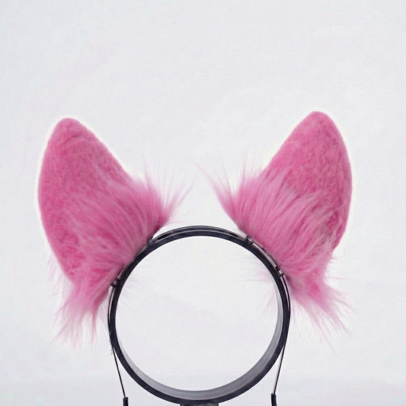 Op de afbeelding: Een hoofdband met een paar roze, pluizige kattenoren. De oren zijn felroze en hebben een zachte, harige textuur. De hoofdband is zwart en gemaakt van plastic, ontworpen om op het hoofd te worden gedragen.