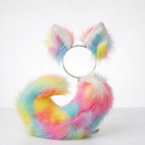 May include: A vibrant costume set comprising a headband with fluffy ears and a tail. The ears and tail are a blend of pastel shades: pink, yellow, blue, and white. This set is intended as a costume accessory, perfect for themed events.