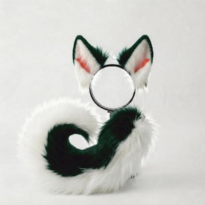 May include: A furry costume set featuring a pair of white and green fox ears and a matching tail. The ears have a black headband and red inner ear detail. The tail is white with a dark green stripe.