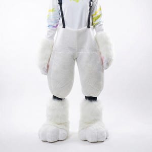 May include: A white furry costume featuring large trousers, mittens, and foot covers. The costume has black braces and is worn over a white long-sleeved top with colourful accents. The foot covers are designed to resemble paws.