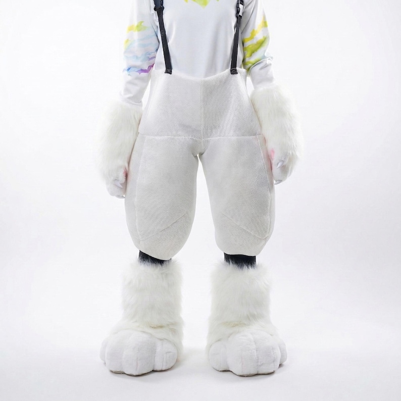 May include: A white furry costume with oversized pants, mittens, and foot covers. The costume has black suspenders and is worn over a white long-sleeved shirt with colorful accents. The foot covers have a paw-like design.