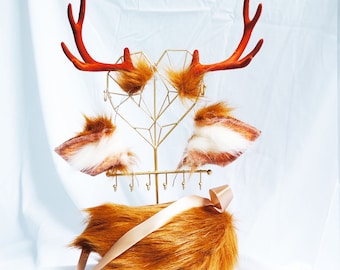 May include: A gold heart-shaped jewelry stand with two antlers and three faux fur tails. The tails are brown, white, and a mix of brown and white.