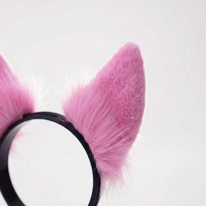 Op de afbeelding: Een zwarte haarband met twee roze, pluizige kattenoren. De oren zijn felroze en hebben een zachte, harige textuur. De haarband is gemaakt van zwart plastic en is ontworpen om comfortabel op het hoofd te passen. Ideaal voor cosplay of kostuumfeesten.