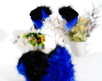 May include: A set of blue and black faux fur cat ears and tail. The ears are attached to a gold wire stand. The tail is fluffy and has a black tip.