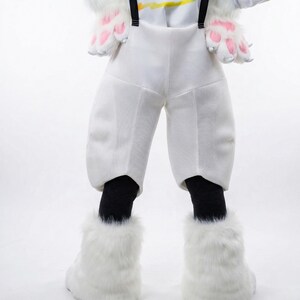 May include: A white costume featuring a pair of white pants with black suspenders, black socks, and fluffy white boots. The costume also includes white gloves with pink paw pads. The outfit is designed to resemble a furry animal.