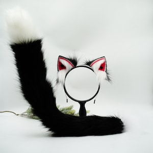 May include: Black and white faux fur tail with a white tip and red-tipped cat ears headband. The headband has a round mirror in the center.