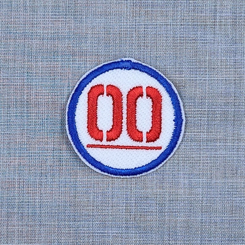 Puede incluir: Un parche circular blanco y azul con un n&uacute;mero "00" bordado en rojo en el centro.