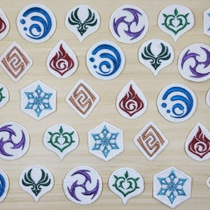 May include: A collection of 18 embroidered iron-on patches featuring various symbols and designs. The patches are white with colorful embroidery. The symbols include a snowflake, a heart, a swirl, a flame, and a bird.