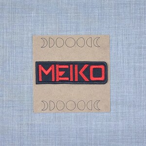 May include: A black and red embroidered patch with the word "MEIKO" in red lettering.