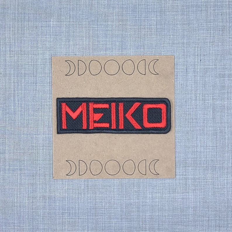 May include: A black and red embroidered patch with the word "MEIKO" in red lettering.