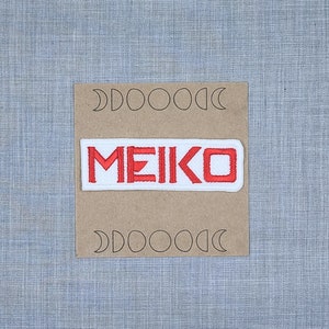May include: White patch with red embroidered text "MEIKO" on a brown background with a pattern of moons.
