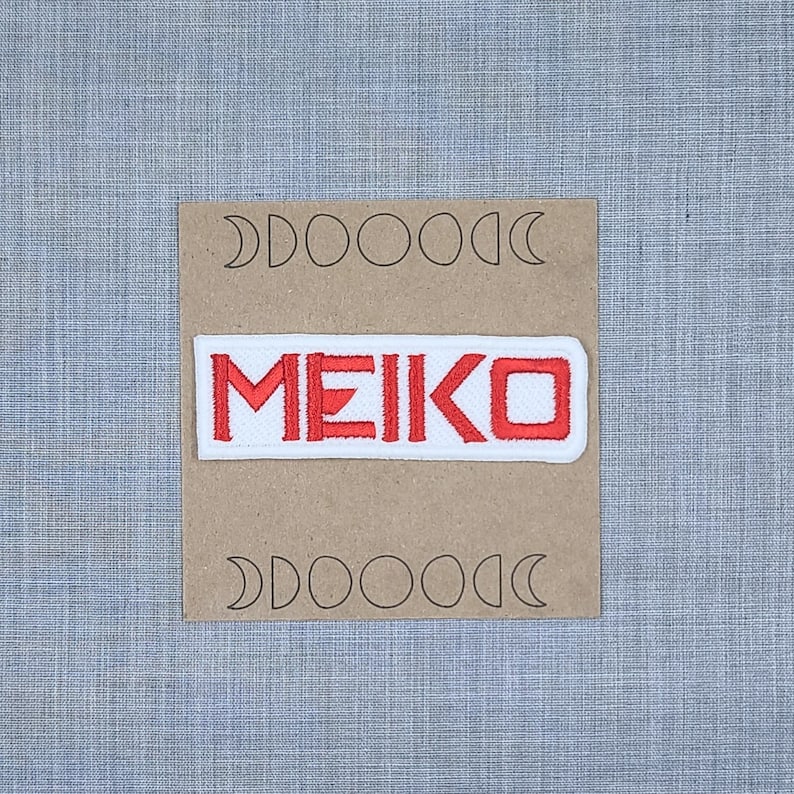 May include: White patch with red embroidered text "MEIKO" on a brown background with a pattern of moons.