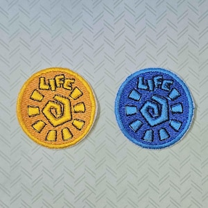May include: Two embroidered iron-on patches with a sun design and the word "LIFE" in a circular shape. One patch is yellow and the other is blue.