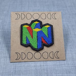 May include: A green, blue, red, and yellow embroidered patch of the Nintendo 64 logo on a brown background.