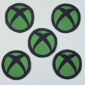 May include: Five circular patches featuring the Xbox logo. Each patch has a green mesh background with a black 'X' design in the center, surrounded by a black border. The patches are arranged on a white surface.