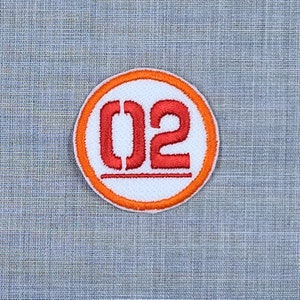 Puede incluir: Un c&iacute;rculo blanco con borde naranja y el n&uacute;mero "02" bordado en rojo.