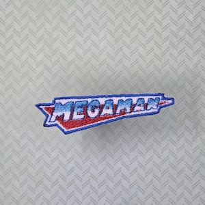 May include: A blue and red embroidered patch with the word "MEGAMAN" in white letters.