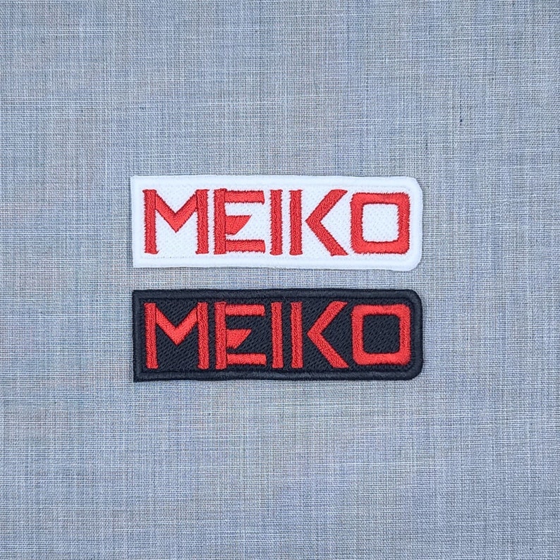 May include: Two embroidered patches with the word "MEIKO" in red lettering. The top patch is white with red lettering. The bottom patch is black with red lettering.