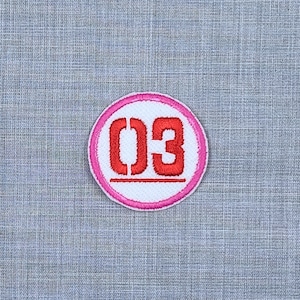 Puede incluir: Un c&iacute;rculo blanco con un borde rosa y el n&uacute;mero "03" en rojo.