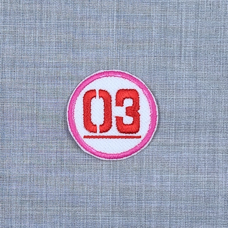 Puede incluir: Un c&iacute;rculo blanco con un borde rosa y el n&uacute;mero "03" en rojo.