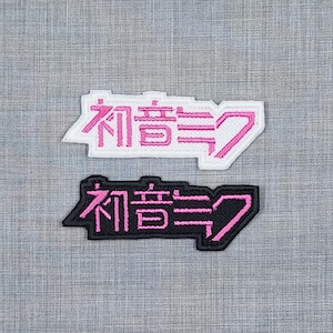 May include: Two embroidered patches with the Japanese text "初音ミク" in pink and black. The top patch is white with pink lettering, and the bottom patch is black with pink lettering.