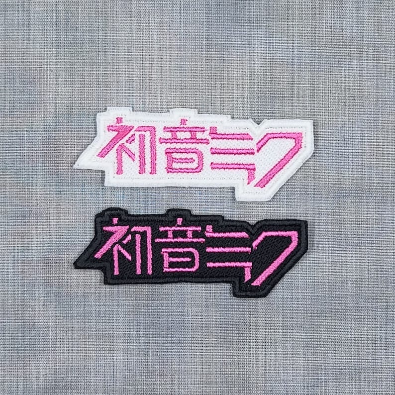 May include: Two embroidered patches with the Japanese text "初音ミク" in pink and black. The top patch is white with pink lettering, and the bottom patch is black with pink lettering.