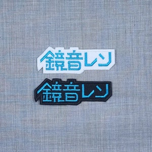 May include: Two embroidered patches with the Japanese text "金曜日" (Kin'yōbi, meaning Friday) in blue lettering. The top patch is white with black outlines, and the bottom patch is black with white outlines.