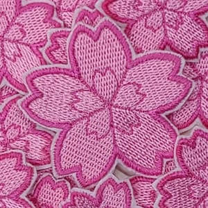 May include: A collection of pink embroidered fabric flower patches. The flowers have five petals and are outlined in a darker pink.