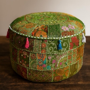 May include: A round, green patchwork ottoman with colourful embroidered details and small tassels. The ottoman is approximately 45 cm in diameter and 30 cm high. The design features various floral and geometric patterns.