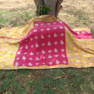 Puede incluir: Una colcha kantha rosa y amarilla con un patrón de paisley. La colcha está doblada y puesta en el suelo.