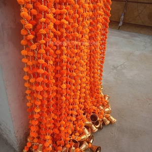 Könnte beinhalten: Orangefarbene und goldene Girlande mit kleinen Glocken. Die Girlande besteht aus Pompons und Perlen.