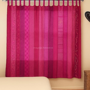 Puede incluir: Una vibrante cortina rosa con rayas verticales. La cortina presenta diferentes tonos de rosa, desde magenta intenso hasta tonos más claros, con bordes decorativos estampados. La parte superior tiene lazos para colgar.